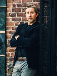 Josh Boldt leaning against brick wall wearing black blazer and t-shirt